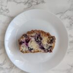 Slice of white loaf cake dotted with blueberries and stopped with crumble.