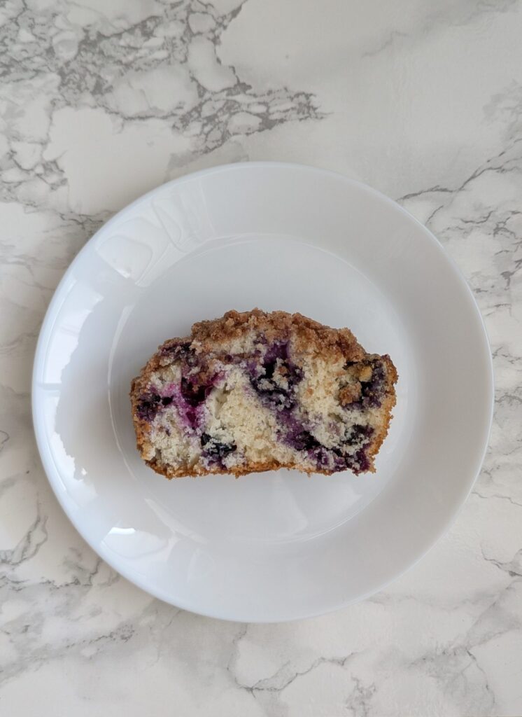 Slice of white loaf cake dotted with blueberries and stopped with crumble.